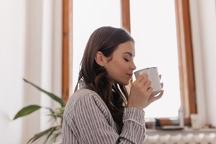 young-woman-striped-shirt-drinks-coffee-from-iron-cup-against-window